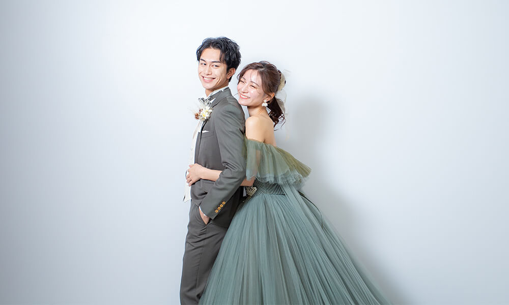 グレーの背景の「マイブライド一宮」のスタジオで洋装フォトを撮影する花嫁と新郎のイメージ