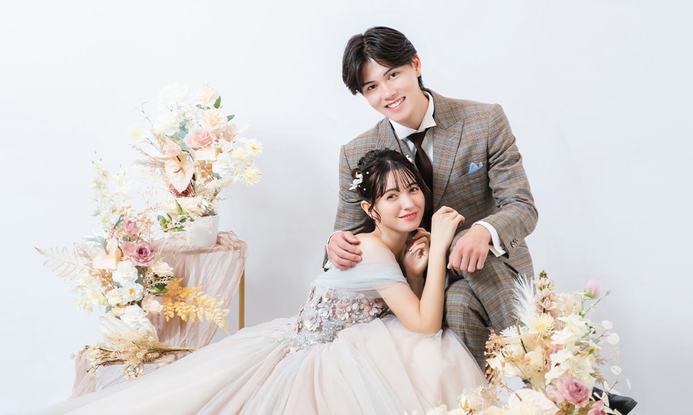 ドライフラワーなどの花が飾られた洋風な空間の「マイブライド春日井」のスタジオで洋装フォトを撮影する花嫁と新郎のイメージ