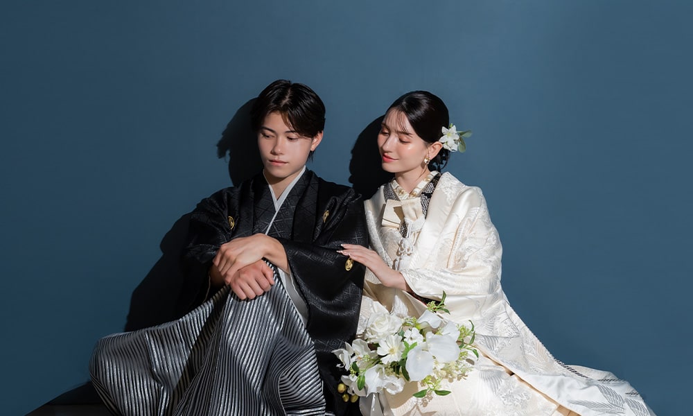 ブルーの背景の「マイブライド春日井」のスタジオで和装フォトを撮影する花嫁と新郎のイメージ