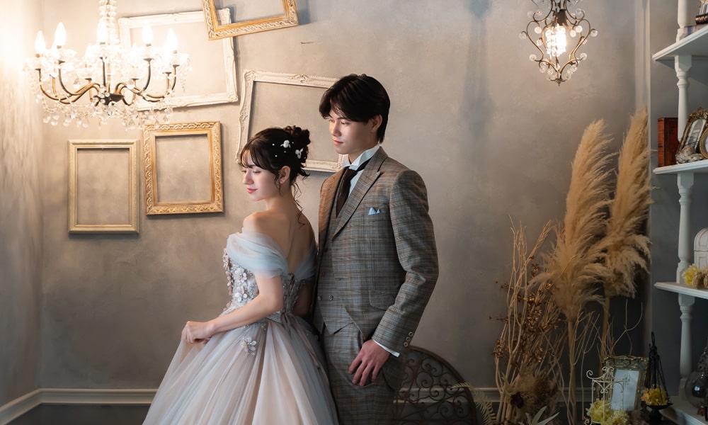 額縁を組み合わせたモチーフに豪華なシャンデリアの光があたる「マイブライド春日井」のスタジオで洋装フォトを撮影する花嫁と新郎のイメージ