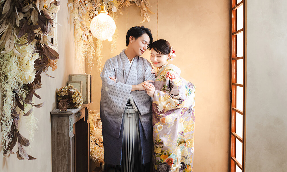アンティークな家具と大きなスワッグのある「マイブライド岡崎光ヶ丘店」のスタジオで和装フォトを撮影する花嫁と新郎のイメージ