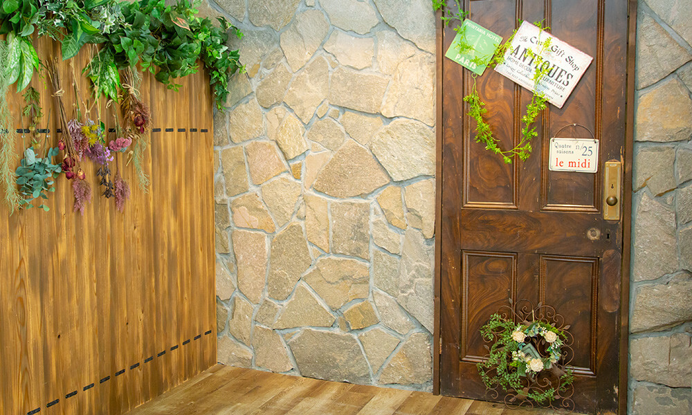 石壁とウッドの壁を背景に木製のドアやドライフラワーなどが配置された「マイブライド尾張旭」のスタジオイメージ