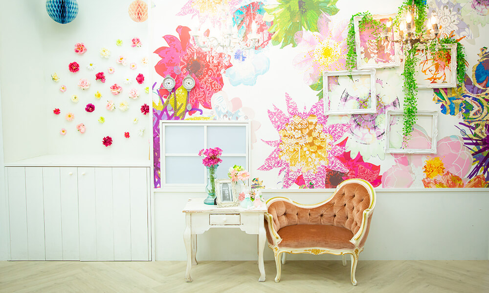 鮮やかな色の花々が描かれた壁に、いろんな額が飾られたアーティスティックな雰囲気のある「マイブライド尾張旭」のスタジオイメージ