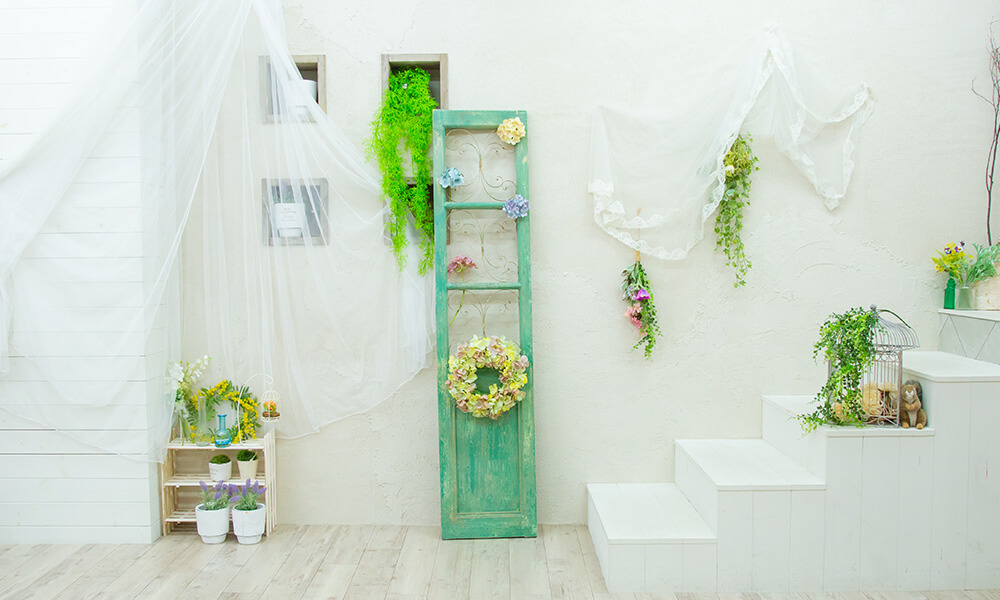 白壁にアンティークなエメラルドグリーンの壁掛けディスプレイやリースなどが配置された「マイブライド尾張旭」のスタジオイメージ