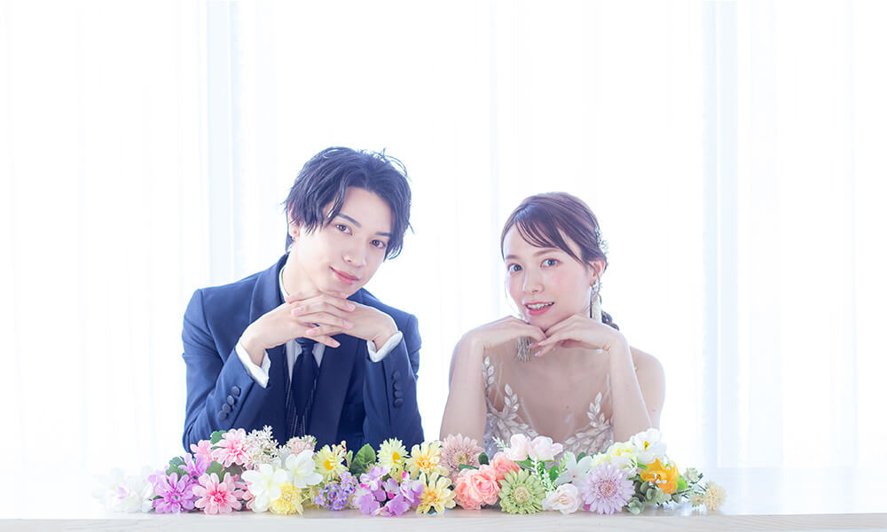 淡い光に包まれる「マイブライド滝ノ水」のスタジオで花を並べて洋装フォトを撮影する花嫁と新郎のイメージ
