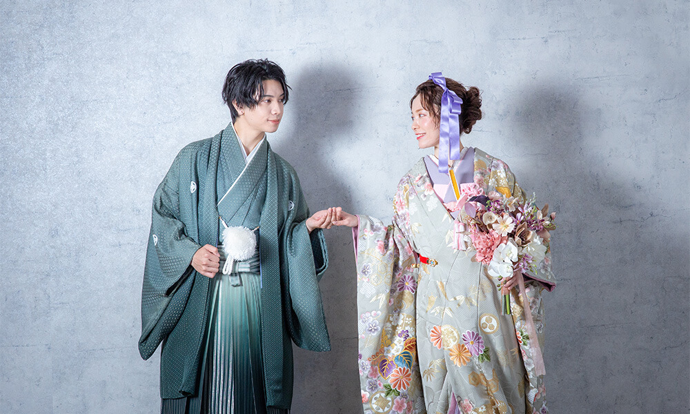 グレーの背景の「マイブライド滝ノ水」のスタジオで手をつないで和装フォトを撮影する花嫁と新郎のイメージ