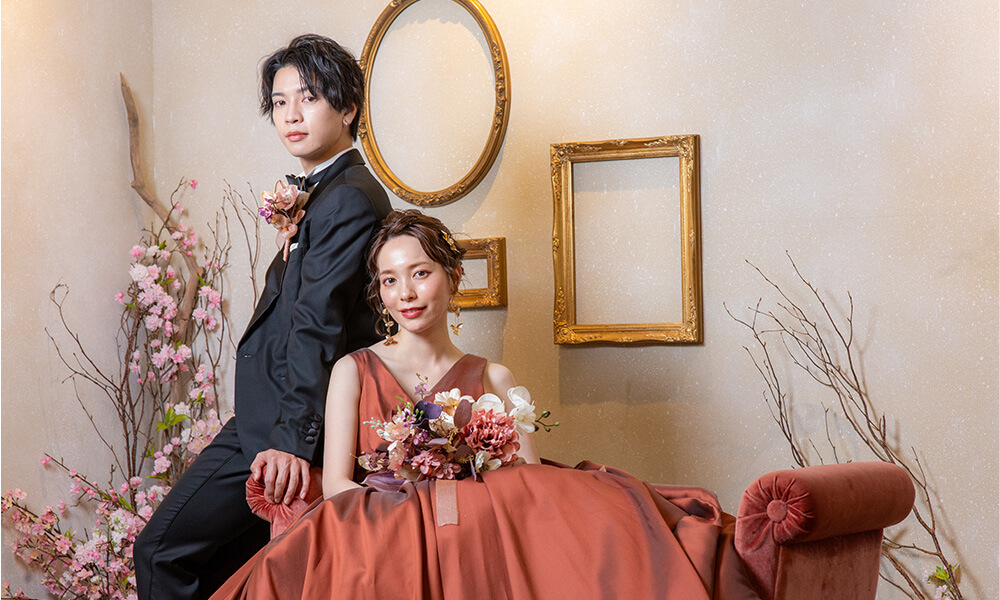 白い背景に洋風な家具を配し、桜のモチーフを散りばめた「マイブライド天白」のスタジオで洋装フォトを撮影する花嫁と新郎のイメージ