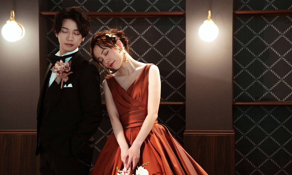 シックな雰囲気の背景の「マイブライド天白」のスタジオで洋装フォトを撮影する花嫁と新郎のイメージ