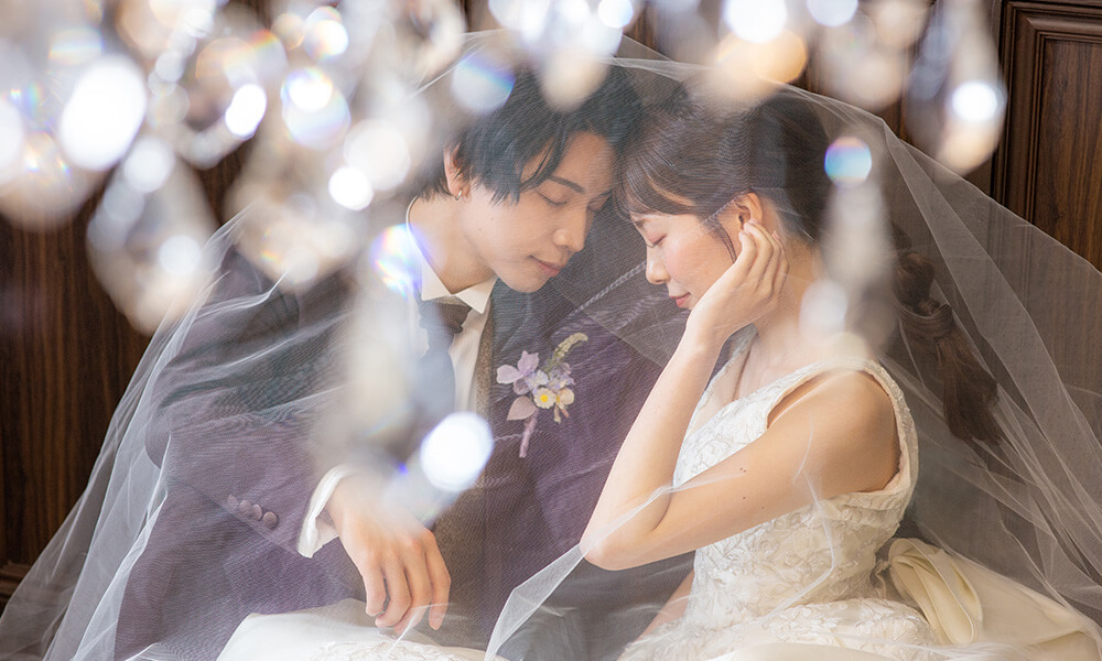 白いレースに包まれながら「マイブライド豊明」のスタジオで洋装フォトを撮影する花嫁と新郎のイメージ