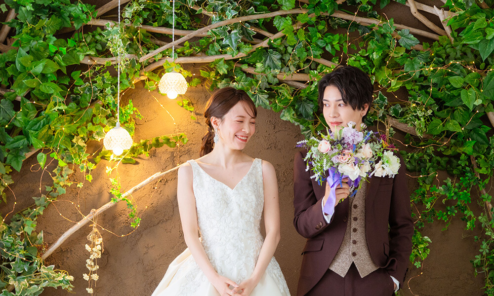 緑豊かな木々とペンダントライトが配置された「マイブライド豊明」のスタジオで洋装フォトを撮影する花嫁と新郎のイメージ