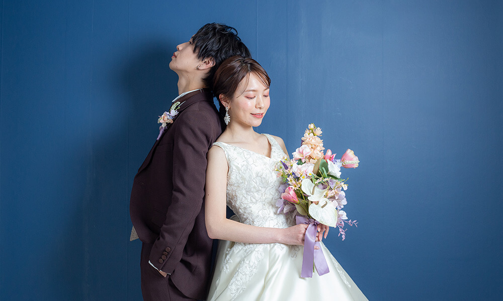 ブルーの背景の「マイブライド豊明」のスタジオで洋装フォトを撮影する花嫁と新郎のイメージ