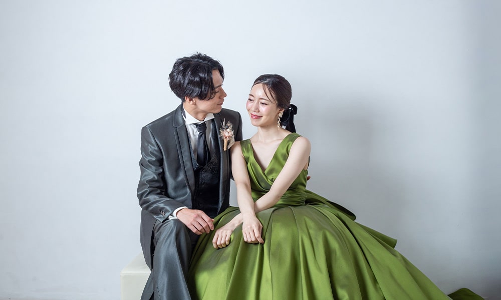 「マイブライド津」のスタジオで、グリーンのドレスを着た花嫁とタキシード姿の新郎が寄り添い座る洋装フォトイメージ